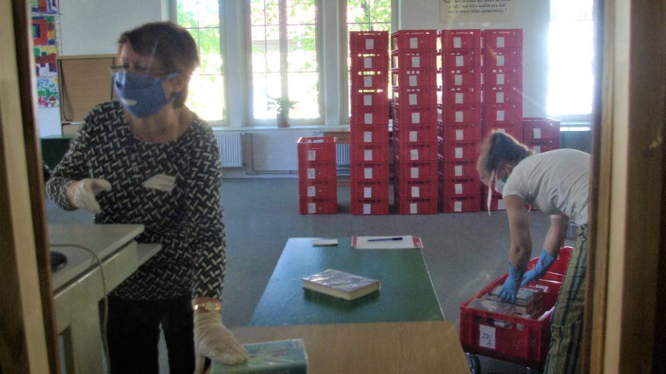 Knihovnice za bezpečnostní přepážkou dávají vrácené knihy do karantény