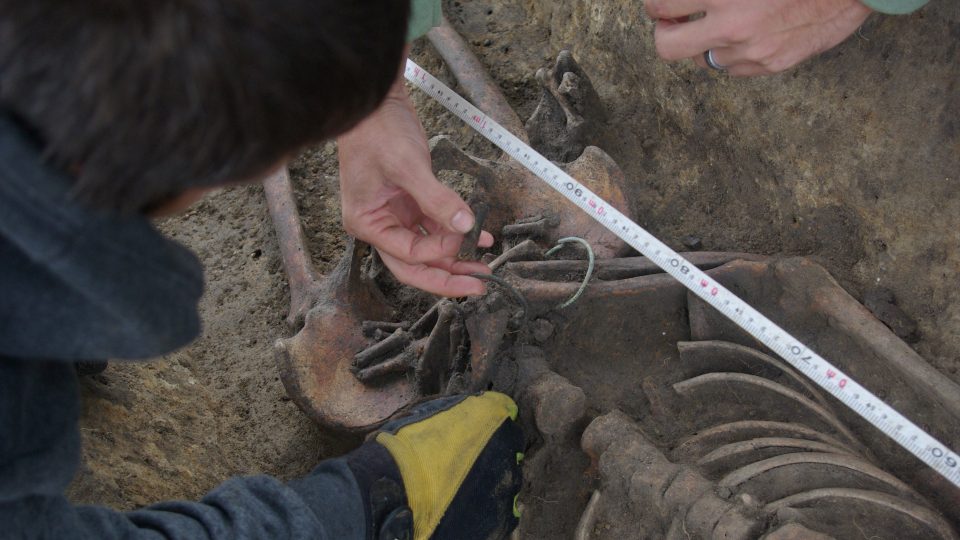 Archeologové z kostry opatrně odebírají bronzové náramky