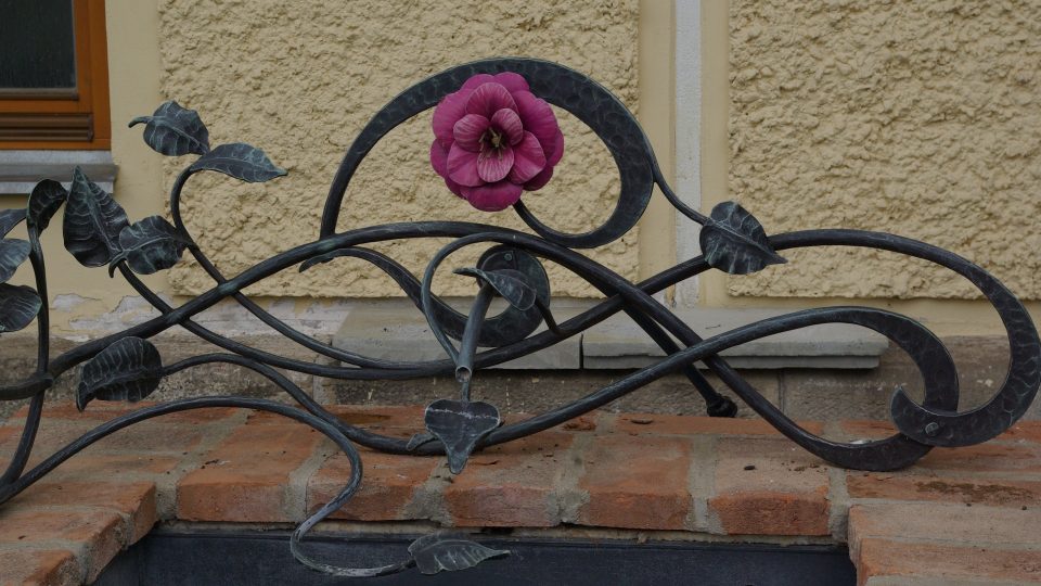 Stylizovaný kovaný květ kamélie odkazuje k botanikovi a jezuitovi Josefu Kamelovi